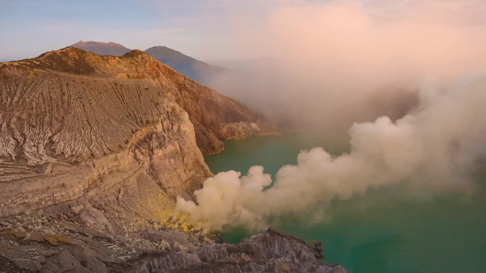 Stunning view of Mount Ijen crater lake at sunrise with teal and orange hues
