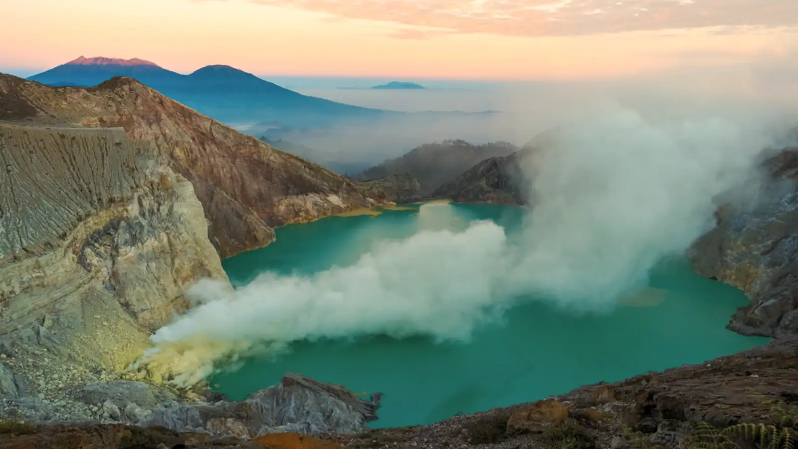 Breathtaking view of Ijen Crater turquoise acid lake and sulfur smoke at sunrise